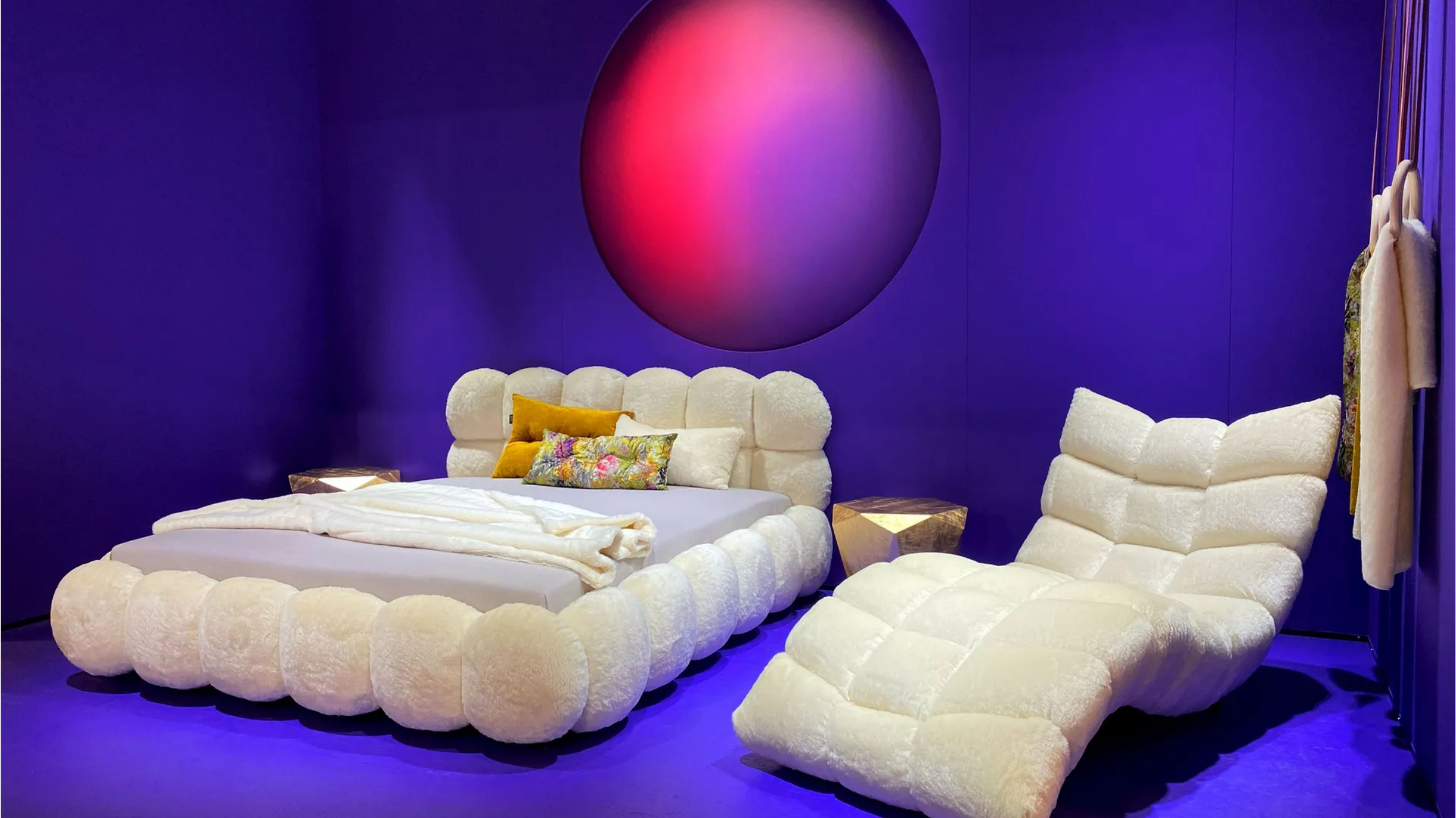Cozy bedroom design featuring a plush bed and lounge chair in a striking purple setting with a round red light.